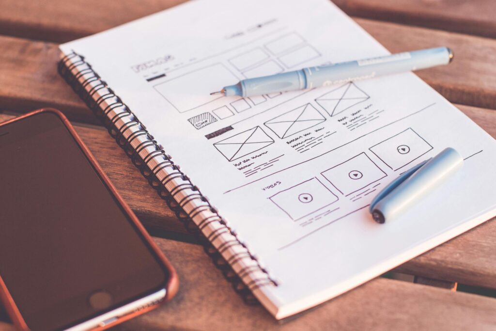 Handgezeichnetes Wireframe auf Notizblock mit Fineliner auf einem Holzschreibtisch – kreativer Startpunkt im authentischen Webdesign